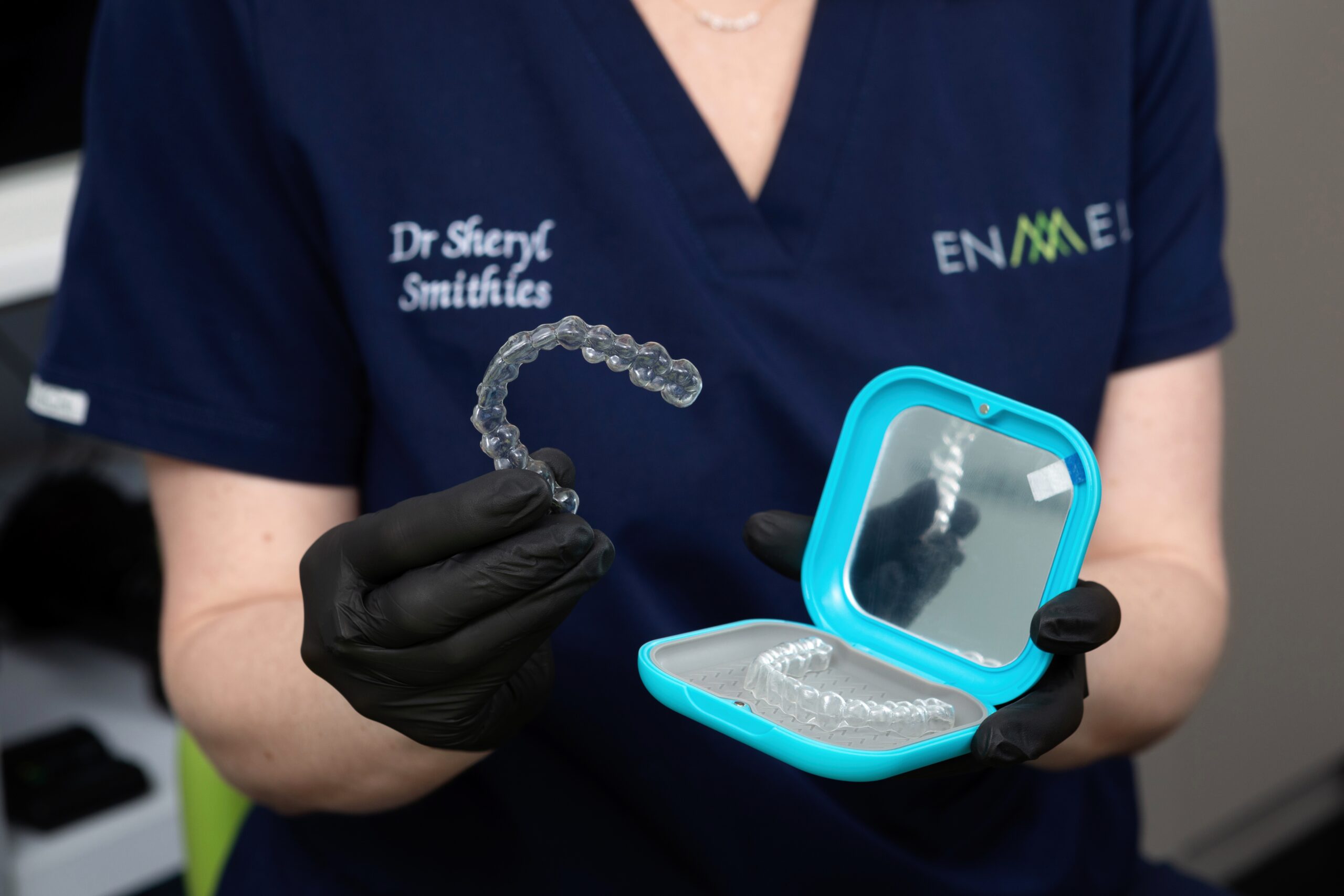 Dr Sheryl Smithies holding a set of clear dental aligners and a turquoise storage case.