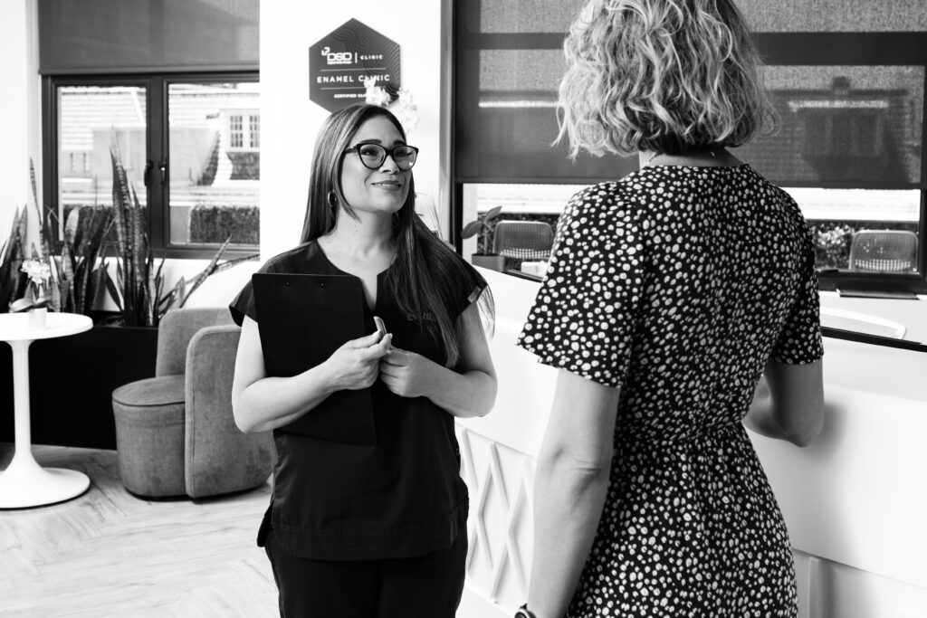 In-house dental coordinator Nikita holding a clipboard and greeting a patient in a bright clinic lounge.